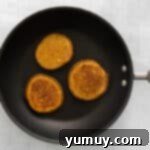 A pumpkin pancake cooking on a griddle, showing bubbles forming on the surface.