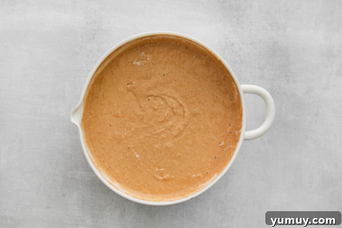 A bowl of pumpkin pancake batter, showing a few small lumps, indicating it has not been overmixed.