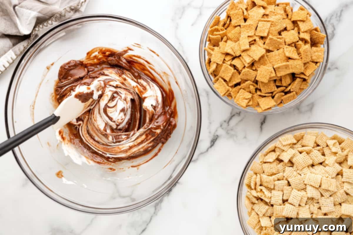 Campfire Crunch Bites 10 marshmallow fluff and butter added to melted chocolate chips in a glass bowl with a rubber spatula.
