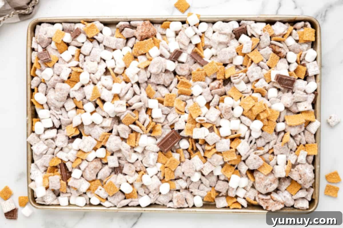 Campfire Crunch Bites 14 chocolate pieces and mini marshmallows added to s'mores puppy chow on a lined baking sheet.