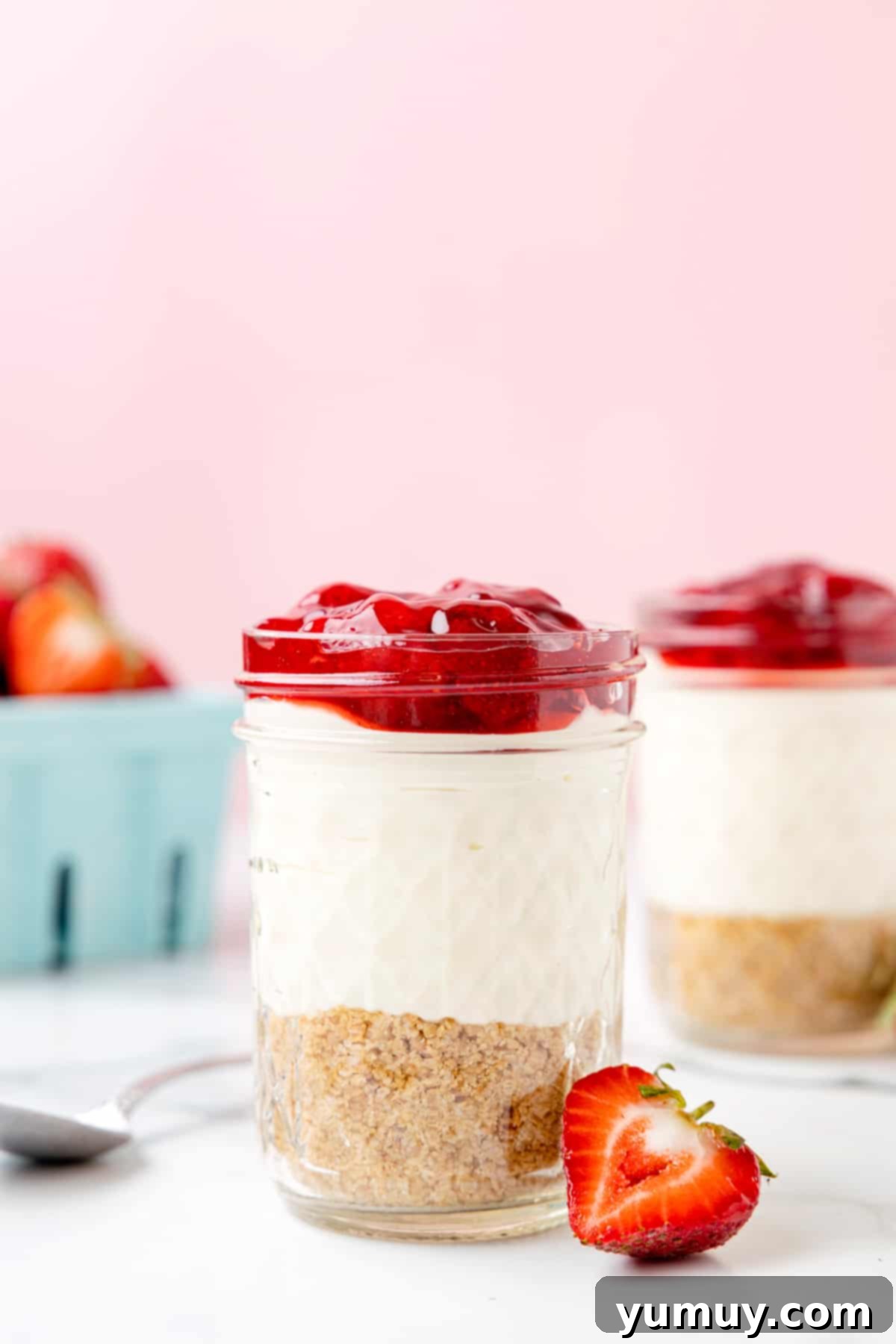 A close-up of a vibrant no-bake strawberry cheesecake cup, showcasing the layers of crust, creamy filling, and bright red strawberry topping.