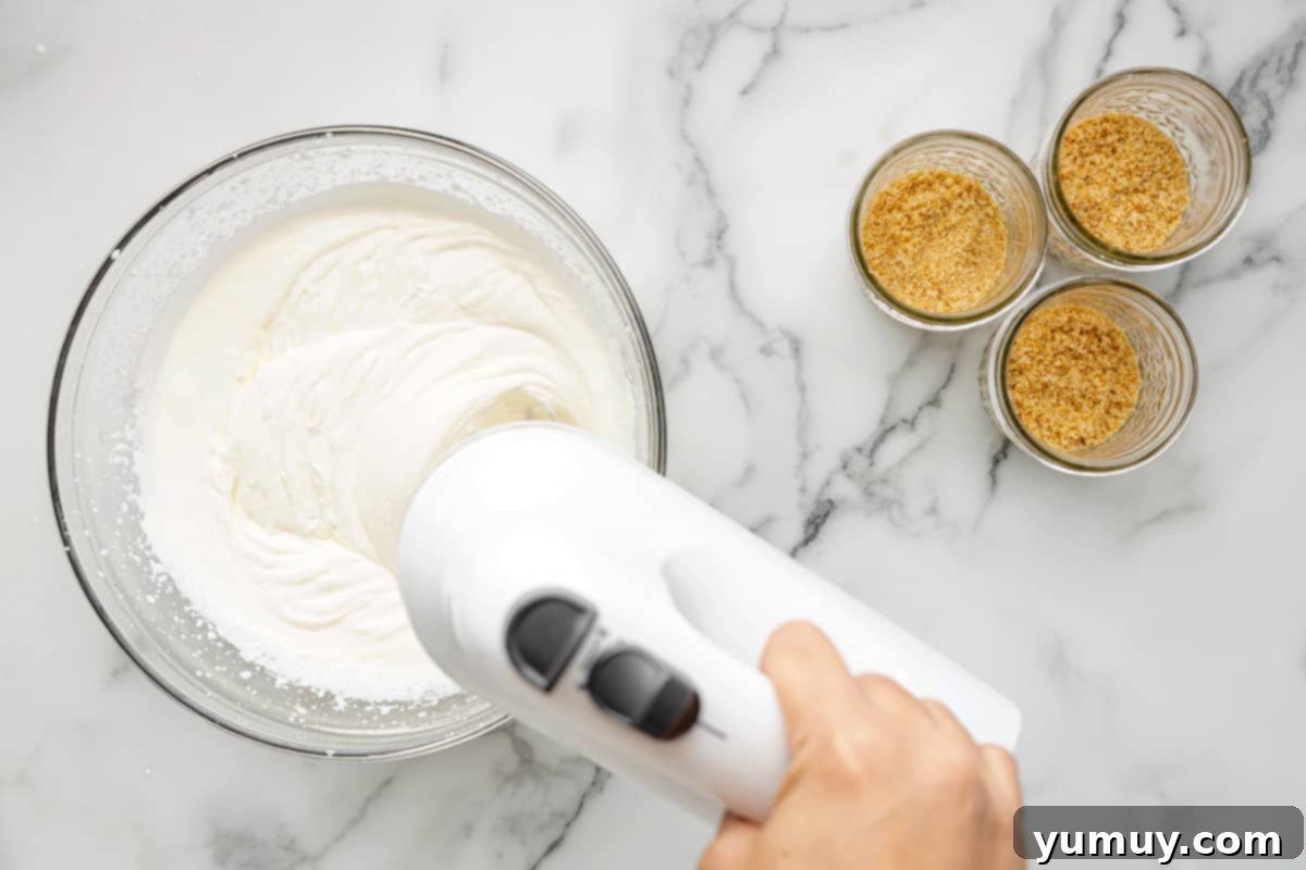 A person expertly using a hand mixer to blend cream cheese, powdered sugar, and vanilla extract until the mixture is soft and creamy.