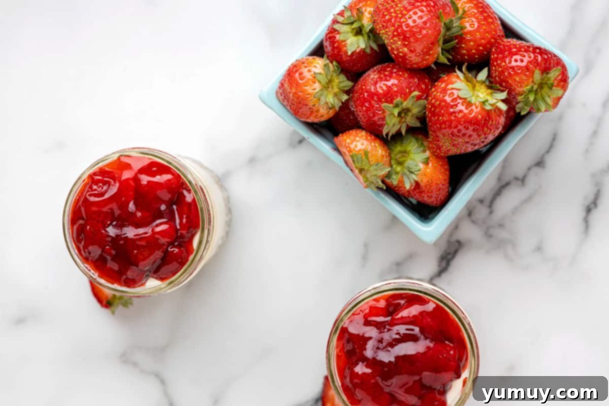 Two finished strawberry cheesecake jars on a marble table, topped with rich strawberry pie filling, ready to be enjoyed.