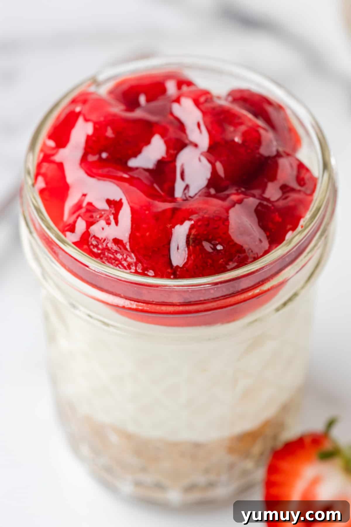 A charming glass jar filled with no-bake strawberry cheesecake, topped with fresh strawberries, ready to be enjoyed.