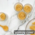 Six glass jars with a layer of pressed graham cracker crust at the bottom.