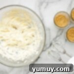 A bowl of heavy cream being whipped with a mixer, showing the formation of soft peaks.