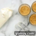 A piping bag dispensing the cheesecake filling into glass jars, creating a smooth layer.