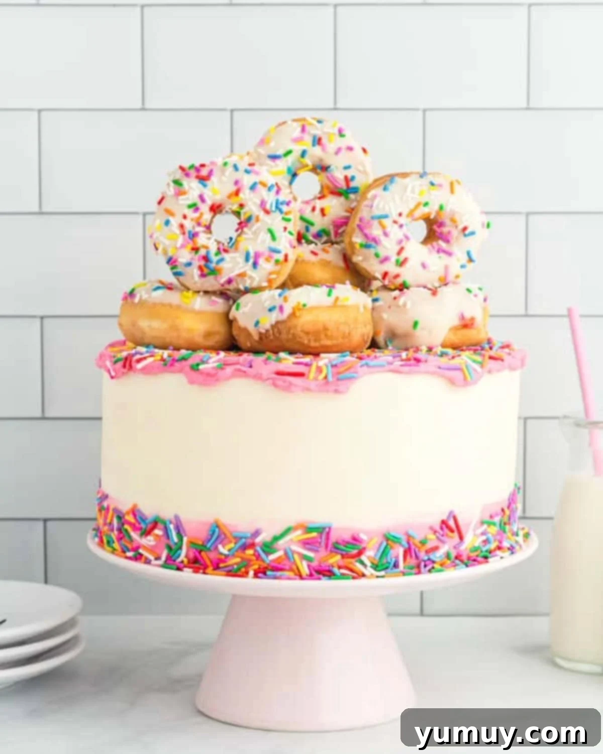 frosted donut cake topped with mini donuts on a cake stand.