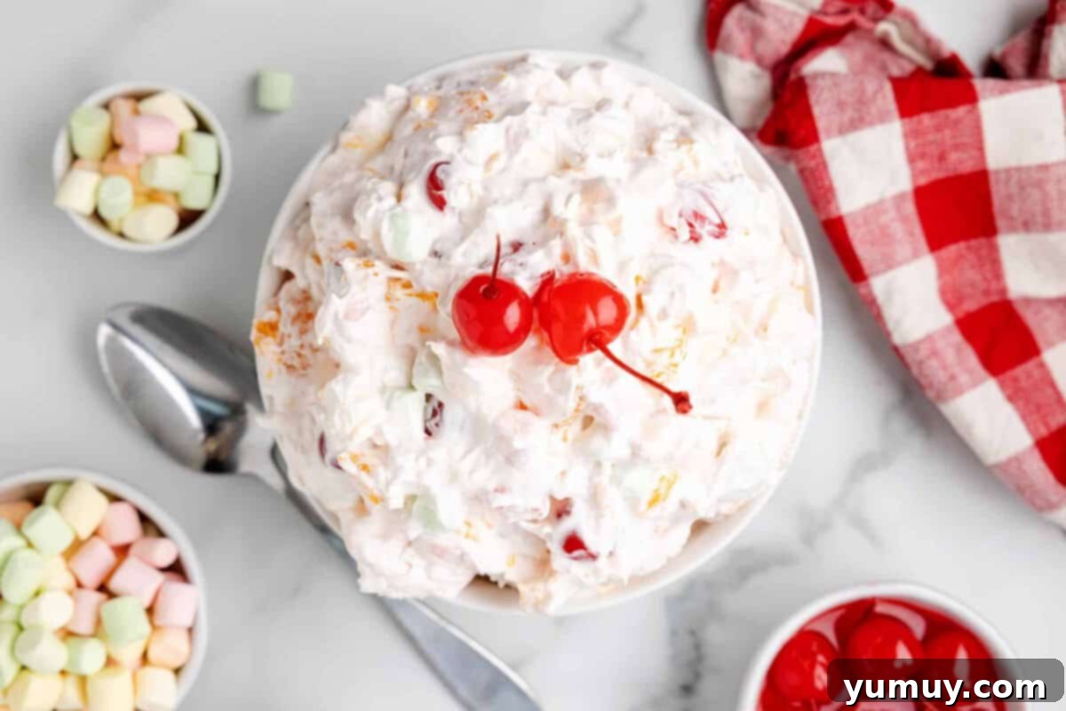 Overhead view of ambrosia salad with two bright maraschino cherries on top in a white serving bowl.