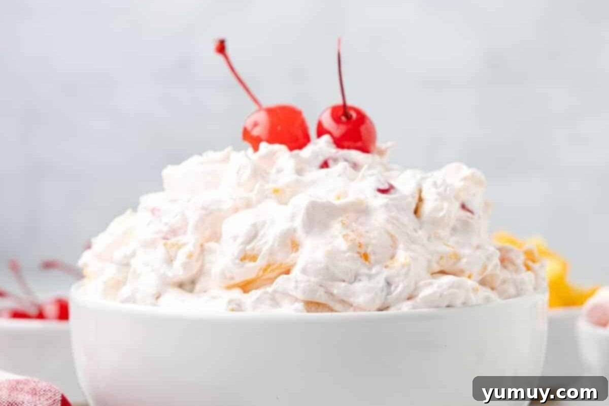 Side view of classic ambrosia salad in a white bowl, garnished with two maraschino cherries on top.