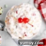 Overhead view of ambrosia salad with two maraschino cherries on top in a white bowl, freshly chilled.