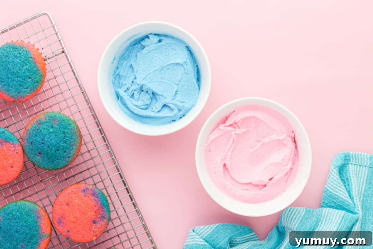 2 bowls of frosting for cotton candy cupcakes in white bowls, one colored blue and one colored pink.