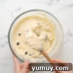 Bursting Blueberry Bundt 11 Stirring blueberries into bundt cake batter in a glass bowl with a rubber spatula.