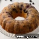 Bursting Blueberry Bundt 13 A freshly baked blueberry bundt cake resting on a glass cake stand, cooling.