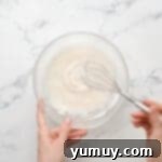 Bursting Blueberry Bundt 14 Vanilla glaze in a glass bowl with a whisk, showing its smooth consistency.
