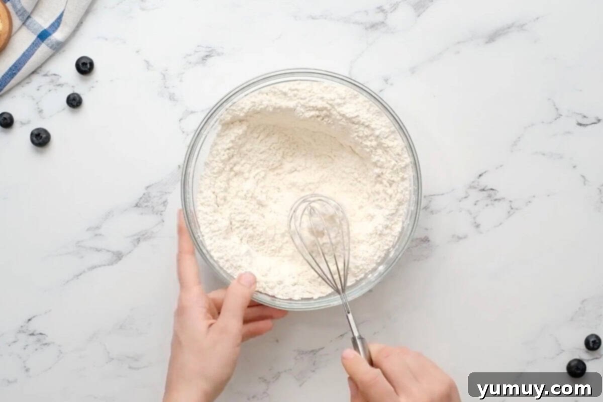 Bursting Blueberry Bundt 17 A glass bowl containing all the dry ingredients for the blueberry bundt cake, mixed with a whisk.