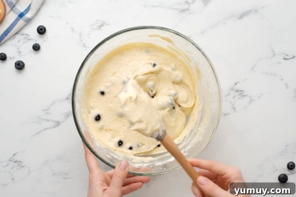 Bursting Blueberry Bundt 19 A rubber spatula gently stirring blueberries into the bundt cake batter in a clear glass bowl.