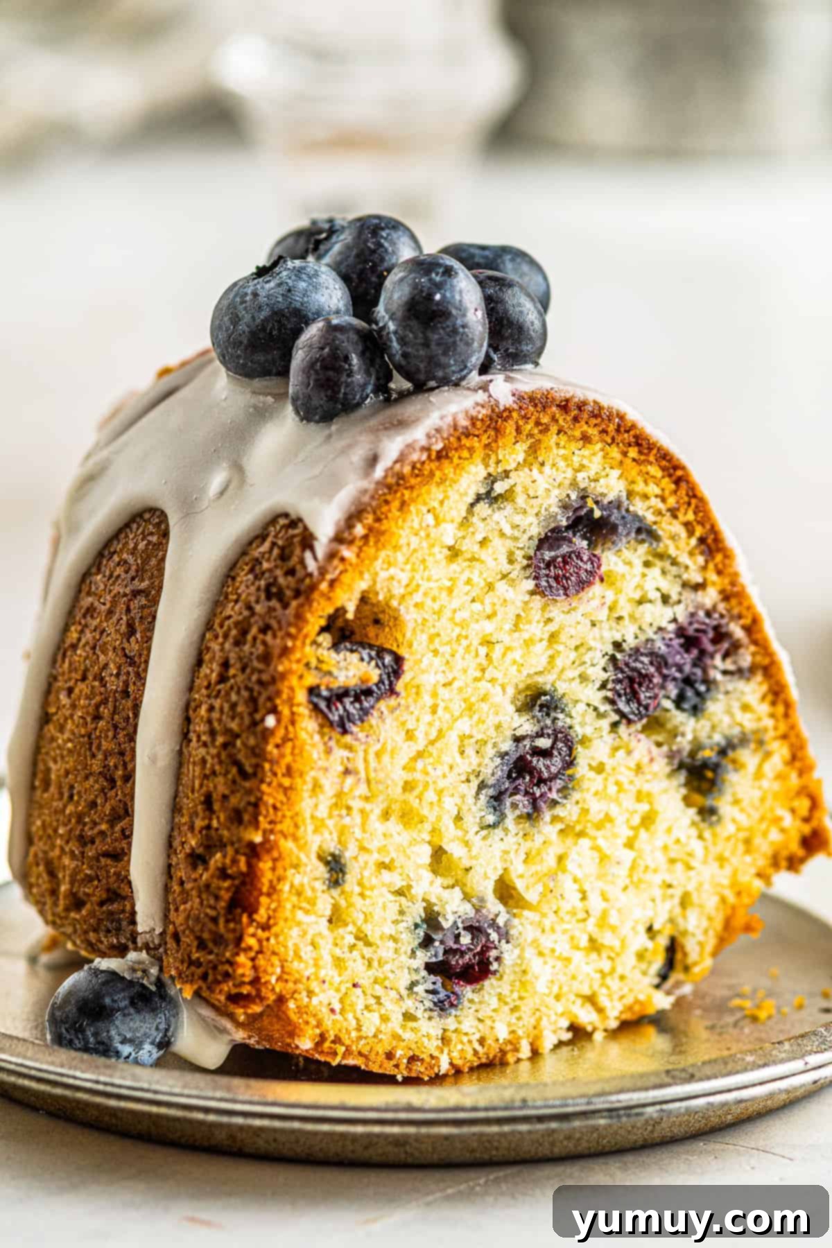 Bursting Blueberry Bundt 3 An inviting close-up of a slice of fresh blueberry bundt cake, showing the moist crumb and juicy blueberries, topped with a delicate glaze.