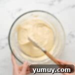 Bursting Blueberry Bundt 10 Folding dry and wet ingredients together to form bundt cake batter in a glass bowl with a rubber spatula.