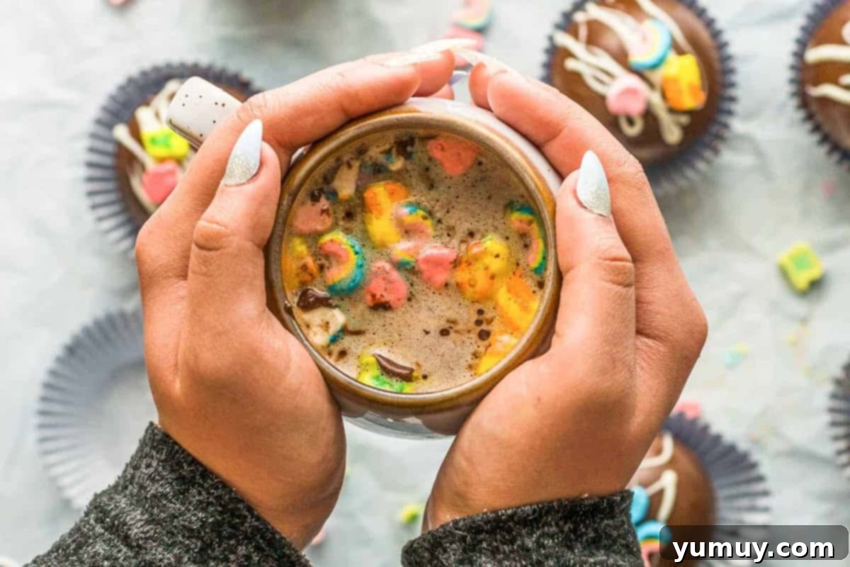 Magical Lucky Charms Hot Cocoa Bombs 3 A pair of hands cupped around a mug containing a dissolving Lucky Charms hot cocoa bomb, with marshmallows floating.