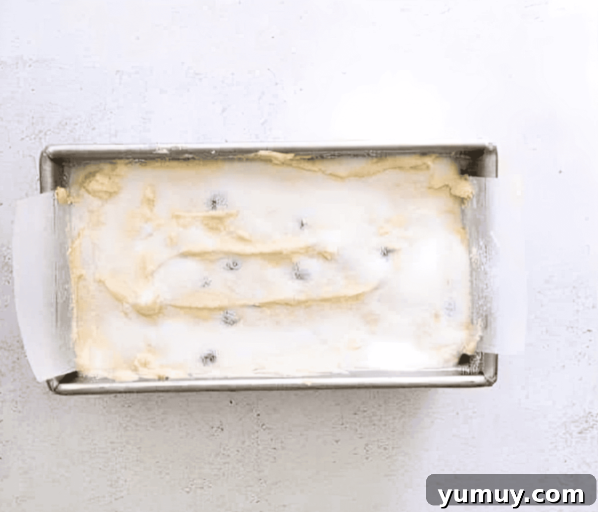 Lemon blueberry pound cake batter evenly spread in a loaf pan, topped with extra sugar, ready for baking.