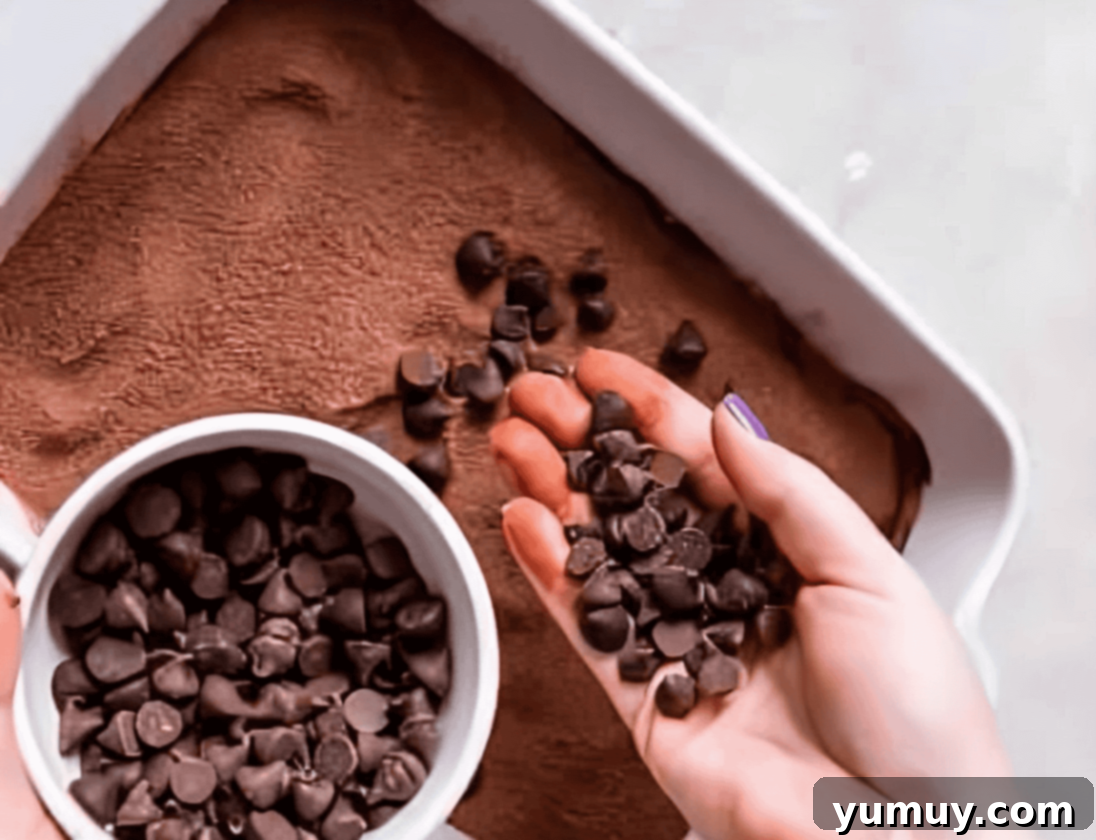 sprinkling chocolate chips over chocolate cobbler batter in a baking dish.