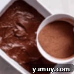 pouring cocoa powder over chocolate cobbler batter in a baking dish.