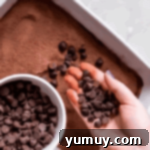 sprinkling chocolate chips over chocolate cobbler batter in a baking dish.