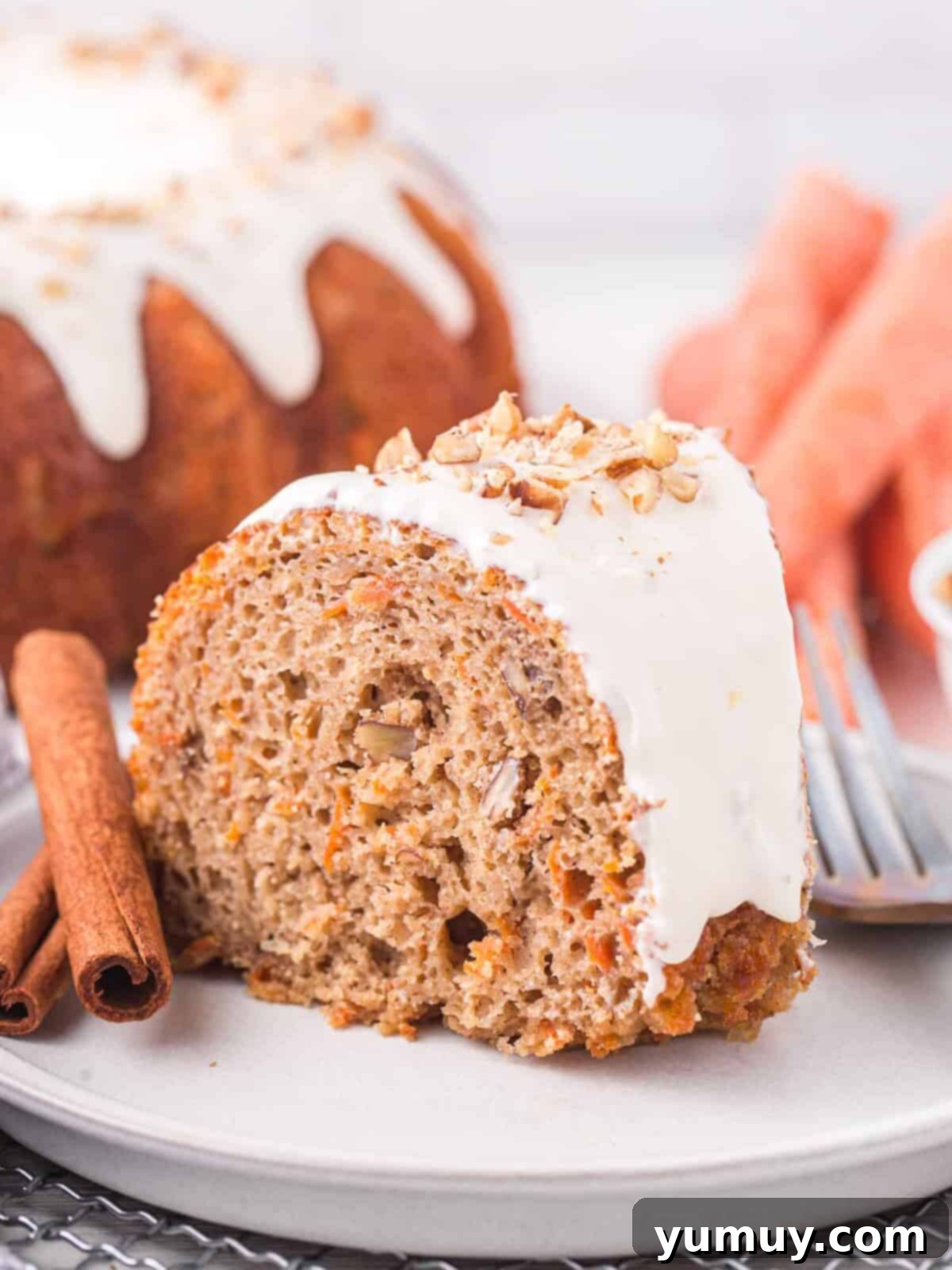 A perfectly sliced piece of moist carrot bundt cake on a white plate, ready to be enjoyed with a fork.