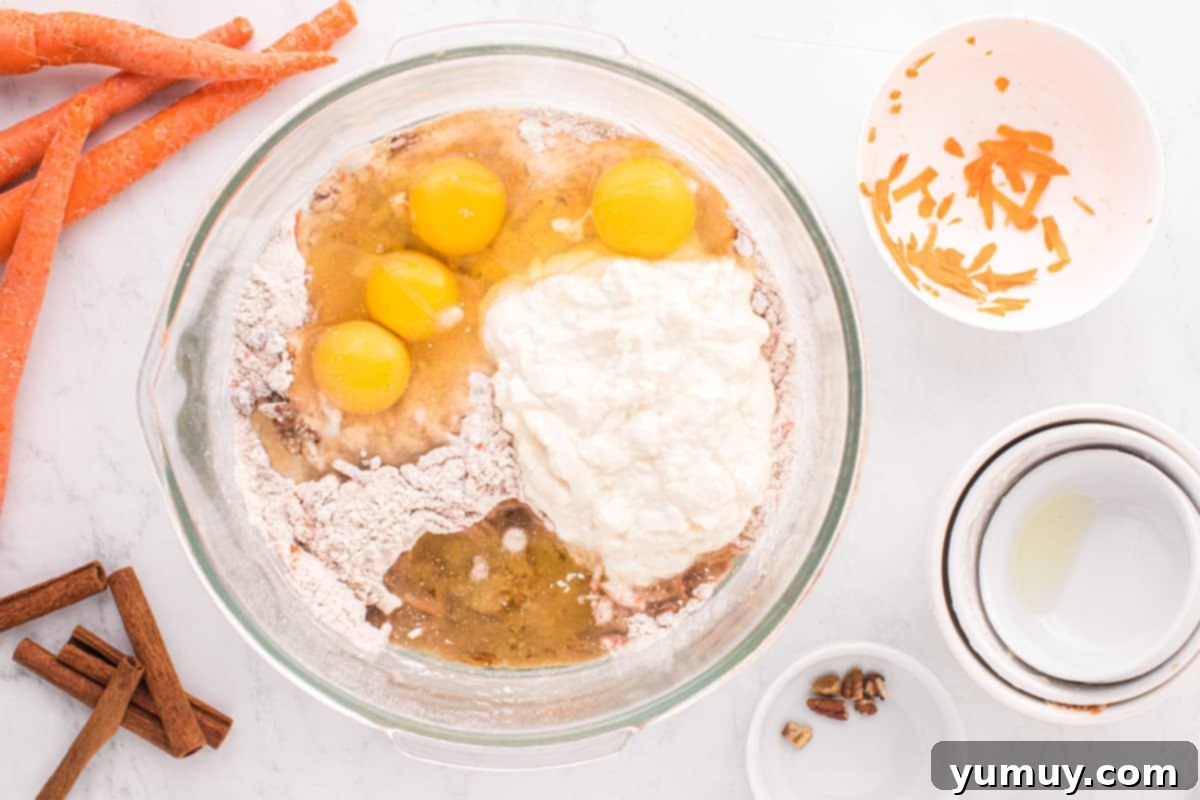 A close-up, overhead perspective of the carrot bundt cake batter, featuring wet ingredients being smoothly blended into the dry mixture in a glass bowl.