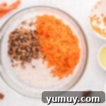 Dry ingredients for carrot bundt cake: cake mix, shredded carrots, and chopped pecans, combined in a clear glass bowl.