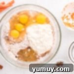 Overhead view of wet and dry ingredients for carrot bundt cake being mixed in a glass bowl to form a smooth batter.