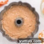 The vibrant carrot bundt cake batter neatly scooped and resting within the contours of a bundt cake pan.