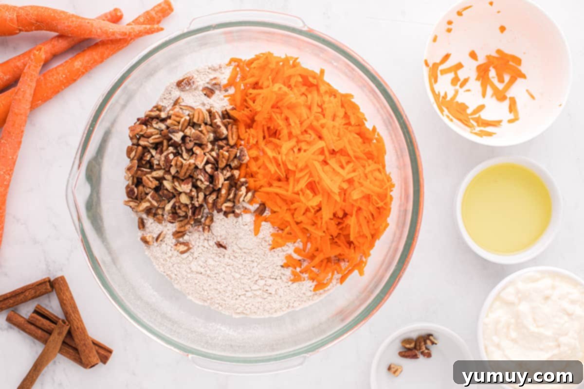 A glass bowl filled with the dry mix for carrot bundt cake, including spice cake mix, shredded carrots, and chopped pecans, ready for wet ingredients.