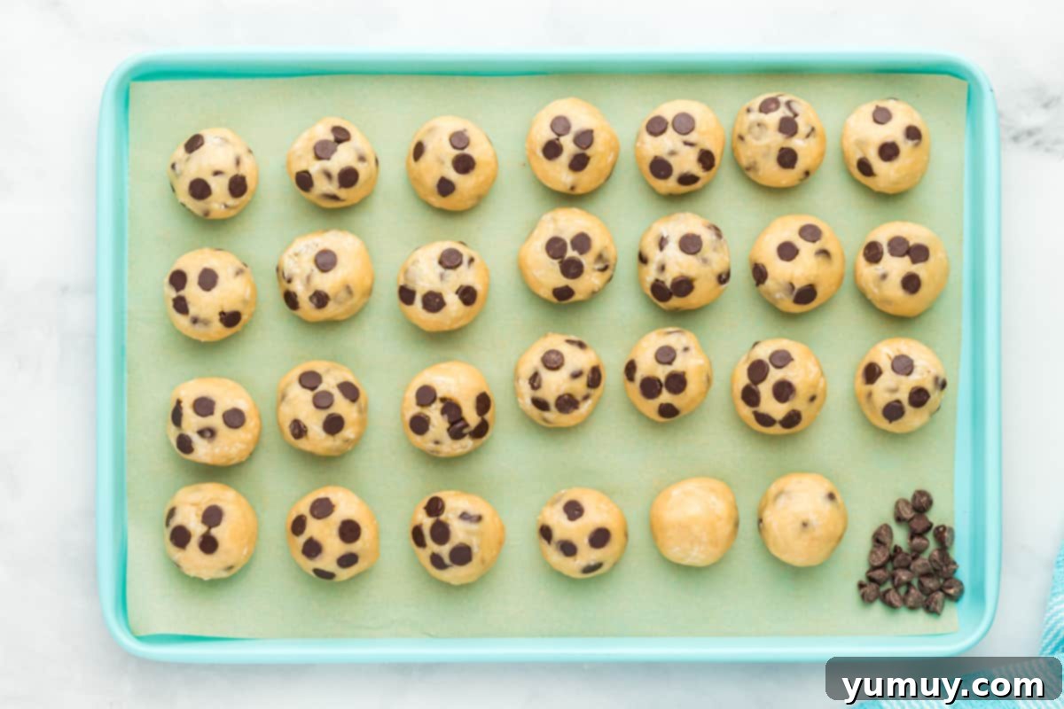 Tropical Coconut Chocolate Chip Delight 15 27 coconut chocolate chip cookie dough balls on a blue baking sheet with chocolate chips pressed into them, ready for chilling.