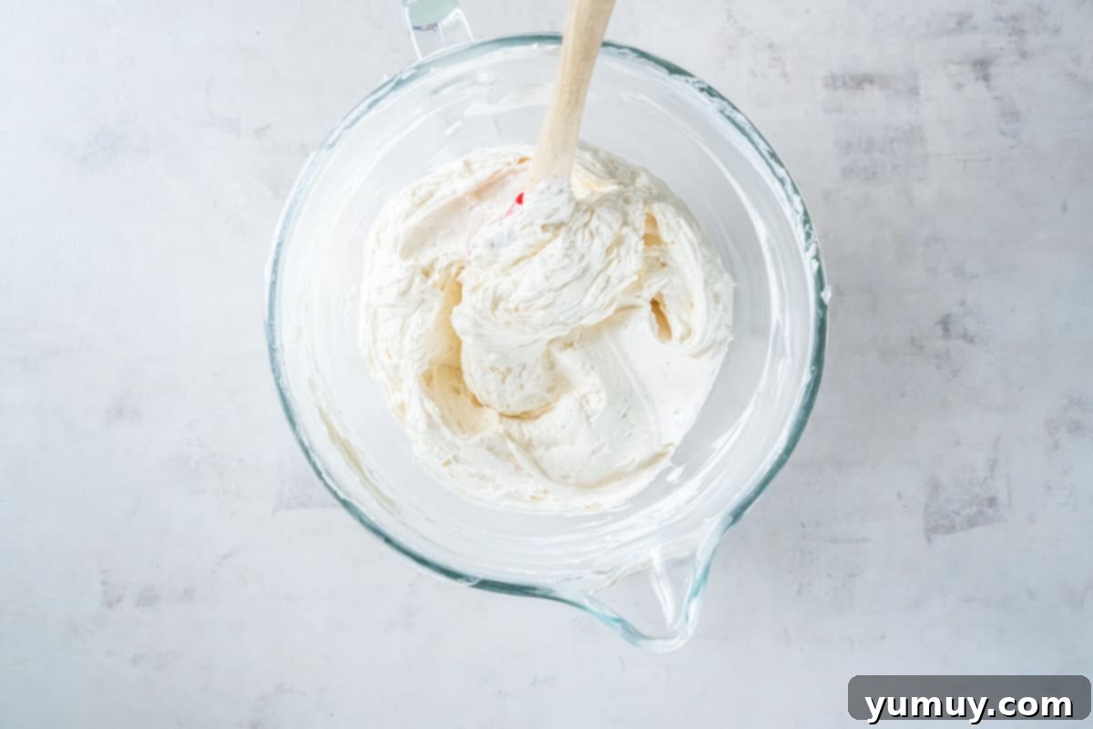 The blended no-bake cheesecake batter, now perfectly folded with whipped topping, rests in a glass bowl alongside a rubber spatula, ready for transfer.