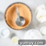 Graham cracker crust being firmly pressed into a springform pan using a measuring cup to create a solid base for the cheesecake.