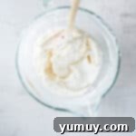 No-bake cheesecake batter, perfectly folded together in a glass mixing bowl with a rubber spatula, showcasing its smooth and creamy texture.