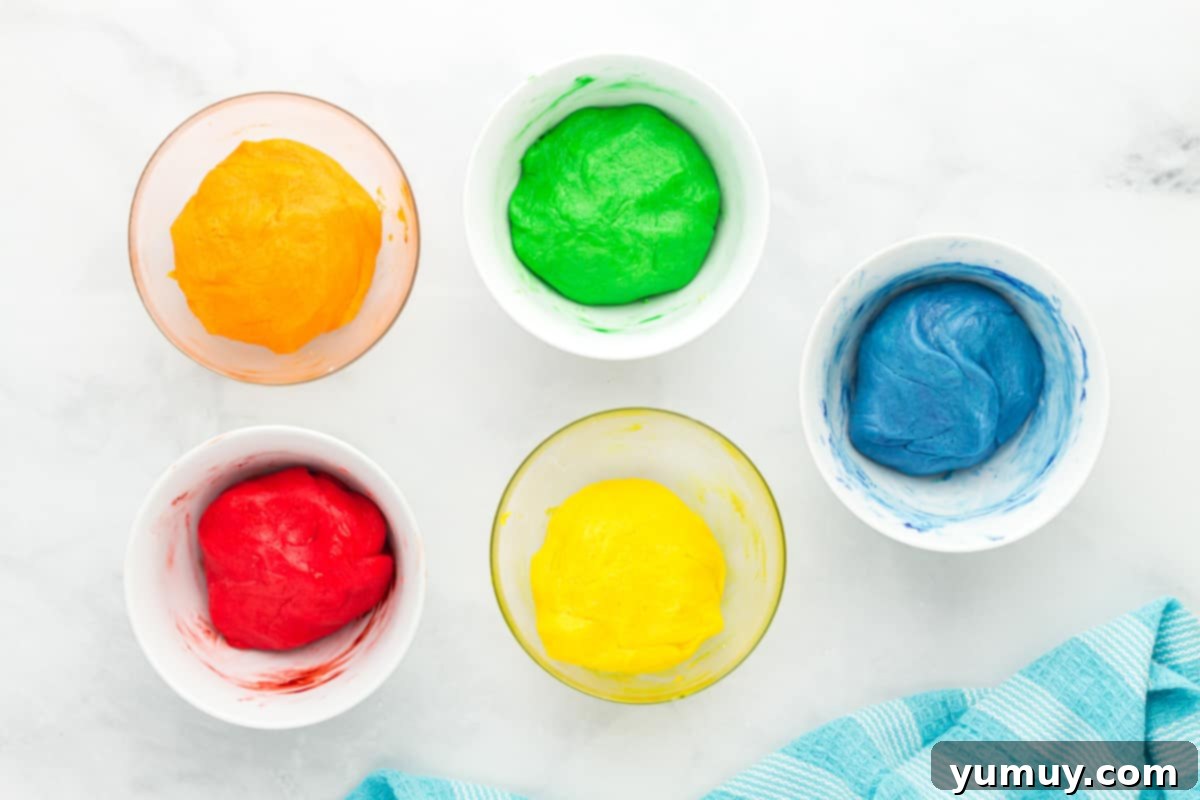 Five brightly colored bowls of Jell-O cookie dough, each a different shade and flavor, mixed and ready.