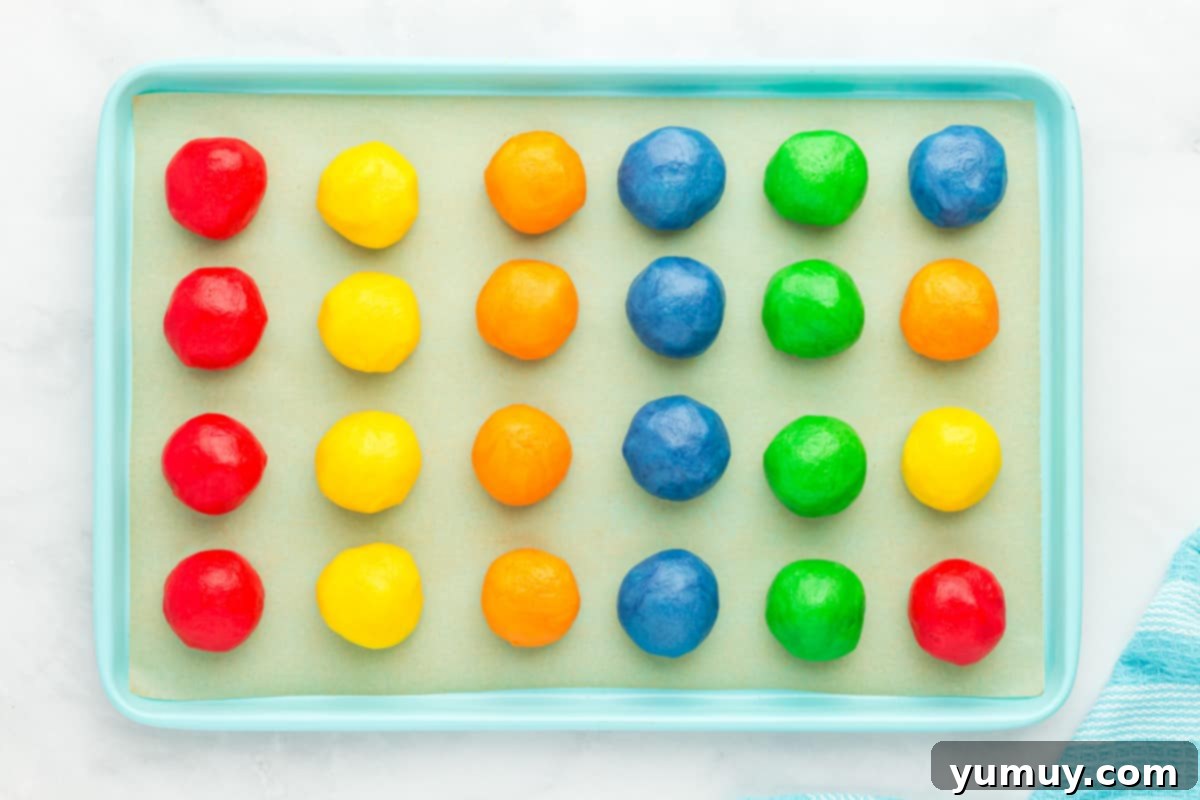 24 perfectly shaped Jell-O cookie dough balls arranged on a blue baking sheet, ready for the freezer.