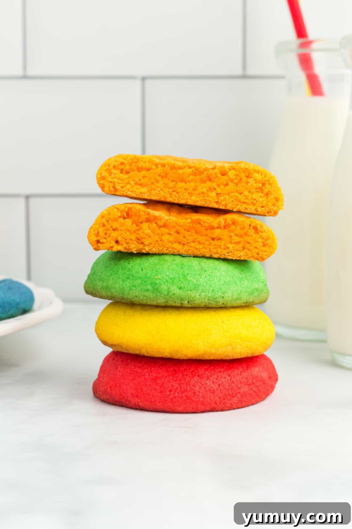 A perfectly halved orange Jello cookie rests atop a colorful stack of red, yellow, and green cookies, revealing its soft, vibrant interior.