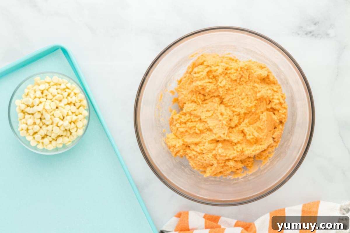 overhead view of orange creamsicle cookie dough in a glass bowl next to a bowl of white chocolate chips.