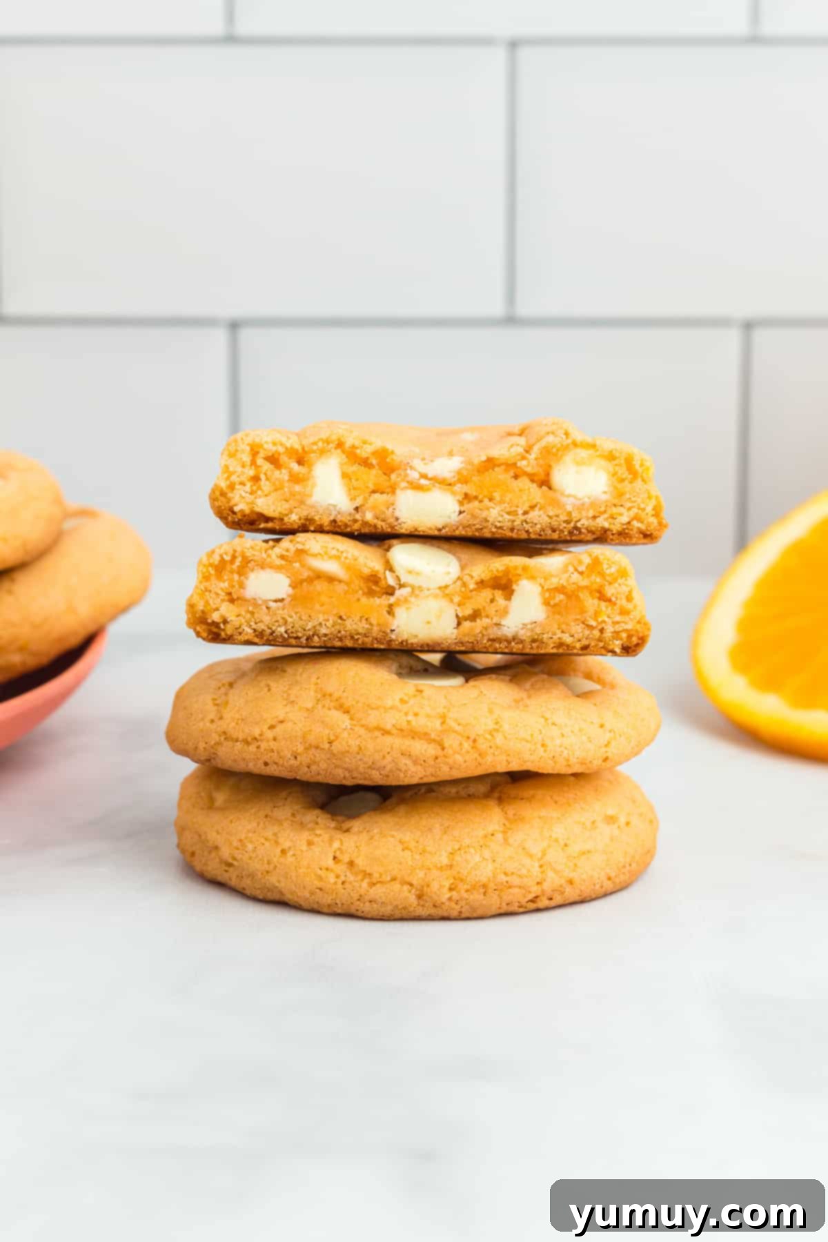 a halved orange creamsicle cookie on top of 2 more cookies showing white chocolate chips inside.