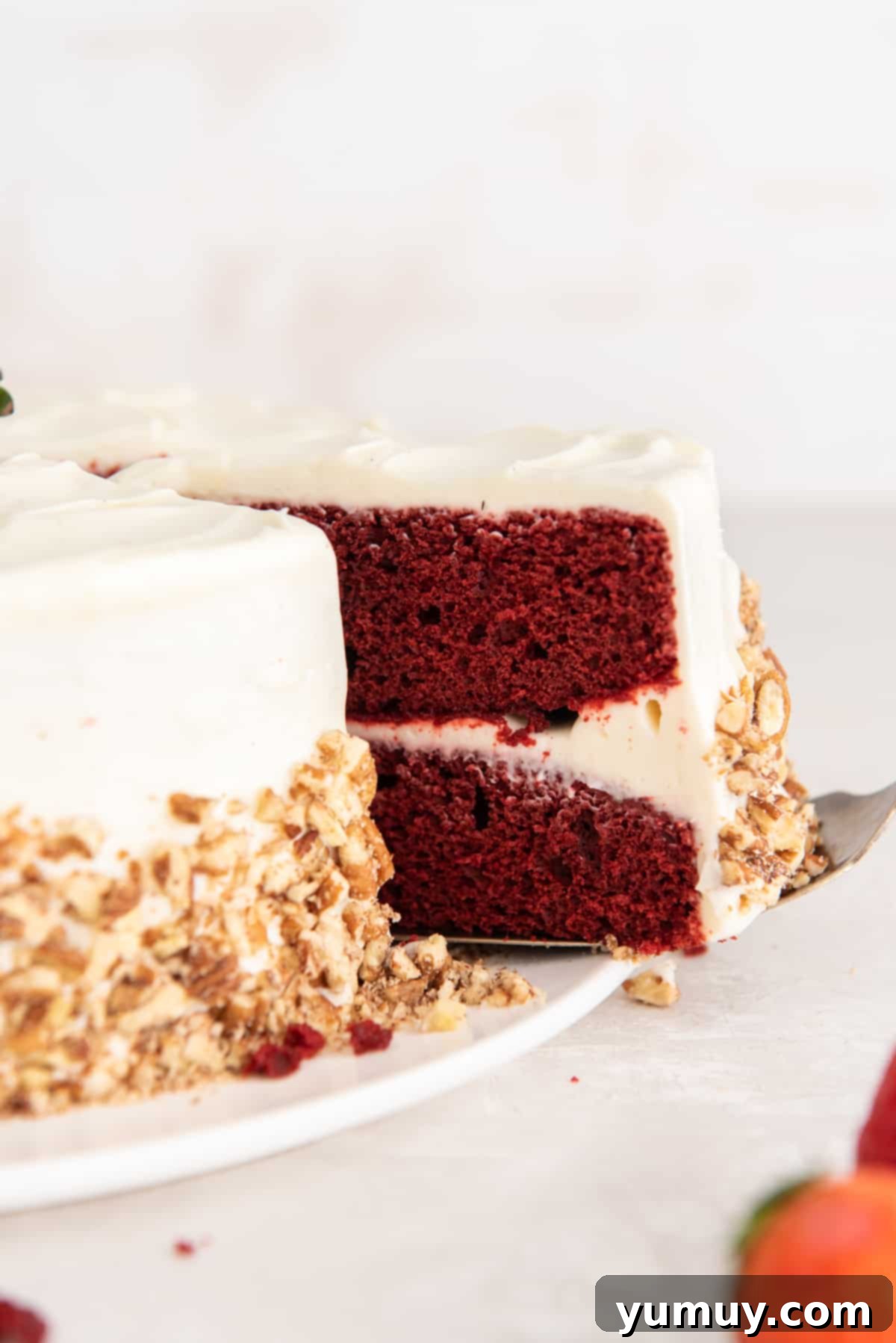 Effortless Red Velvet Cake from a Mix 3 side view of a slice of red velvet cake being removed from a cake on a white cake plate.