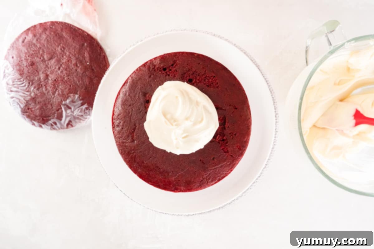 Effortless Red Velvet Cake from a Mix 22 a dollop of cream cheese frosting on a round of red velvet cake on a white cake stand.