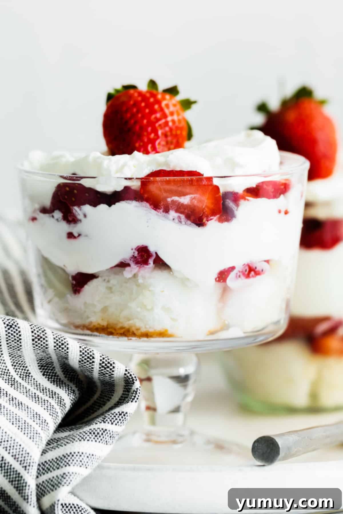 Close-up of a perfectly layered strawberry shortcake trifle in an elegant glass dish, showcasing the vibrant red strawberries, golden cake, and creamy white layers.