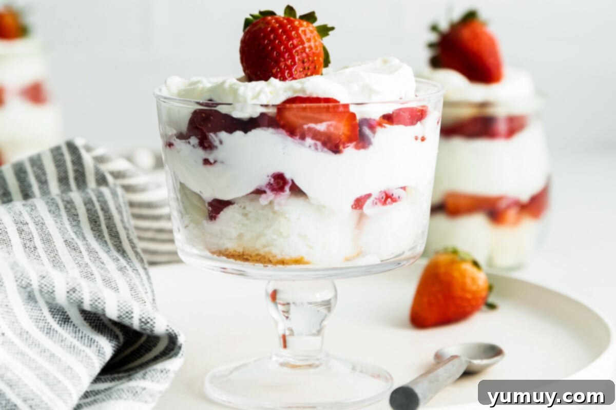 A beautifully assembled strawberry shortcake trifle in a large glass bowl, showcasing the distinct, vibrant layers of cake, strawberries, and whipped cream, ready for serving.
