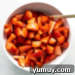 Sliced strawberries, lemon juice, and sugar macerating in a bowl with a spoon, demonstrating the initial step.