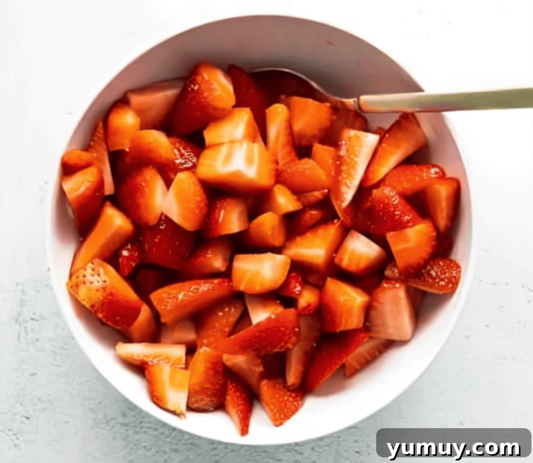Close-up of sliced strawberries, lemon juice, and sugar mixing in a bowl, beginning the maceration process.