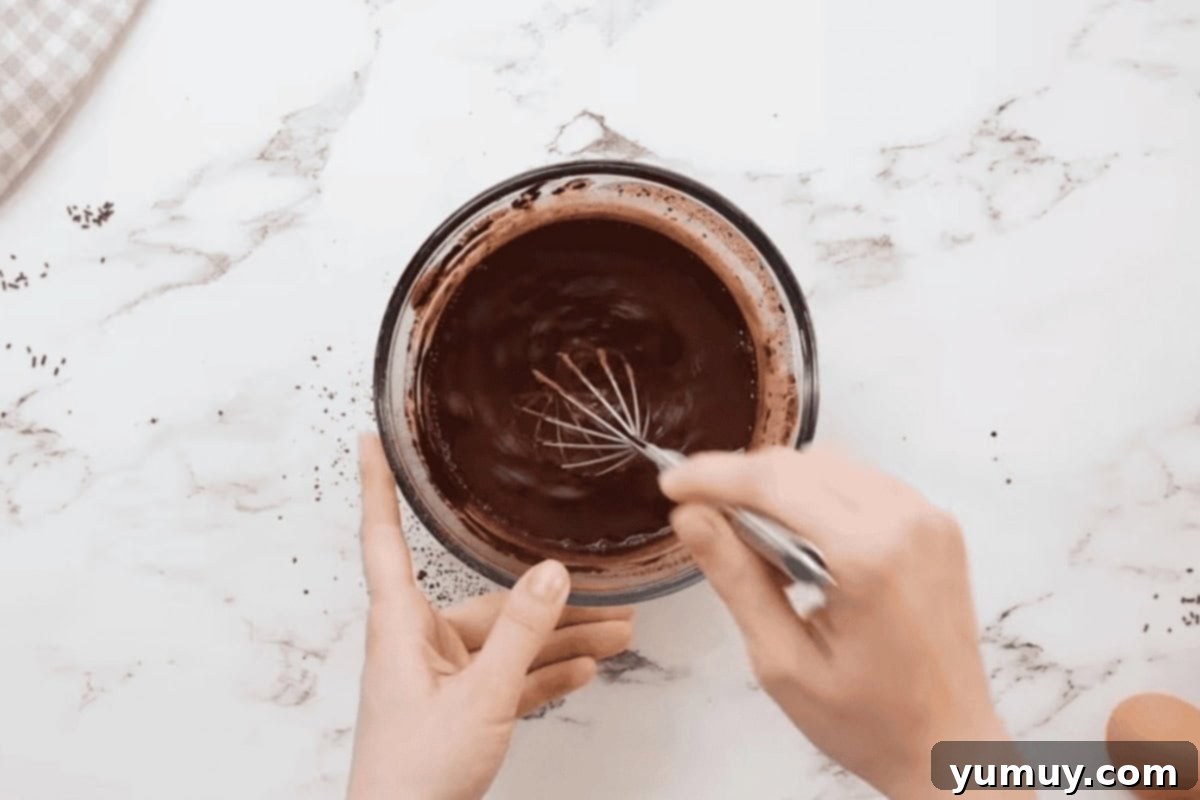 A glass bowl with cocoa powder and boiling water being whisked, illustrating the blooming process.